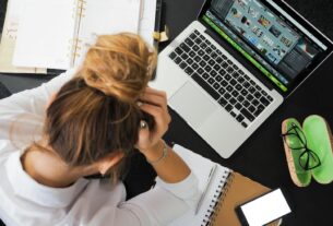 Overhead view of a stressed woman working at a desk with a laptop, phone, and notebooks.