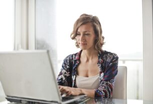 A woman typing on a laptop in a bright, modern home office setting.